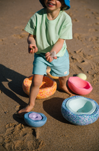 Load image into Gallery viewer, Child enjoying open-ended play with Stapelstein® stones at the shoreline in sand and water.