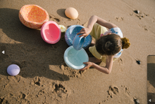 Load image into Gallery viewer, Child using a Stapelstein® stone as a playful seat during beach playtime.