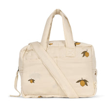 Load image into Gallery viewer, A functional changing bag made of organic cotton, predominantly in a beige color, with lemon printed patterns, an adjustable shoulder strap, and a grab-and-go handle.