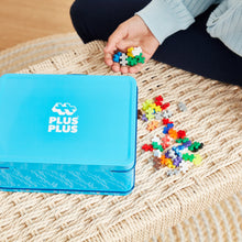 Load image into Gallery viewer, Child playing with colorful building blocks next to a blue Plus Plus box on a woven mat.
